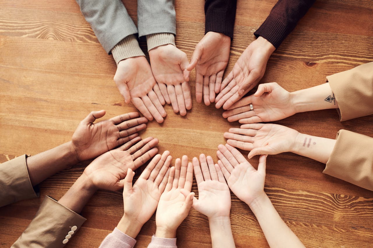 Diverse group of hands joined in circle on wooden table showing unity and teamwork