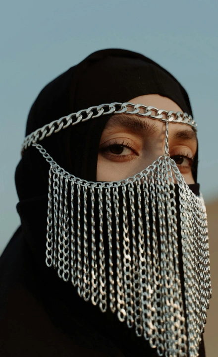 Close-up of a person wearing a black hijab with a silver chain face covering draped over the nose and mouth.