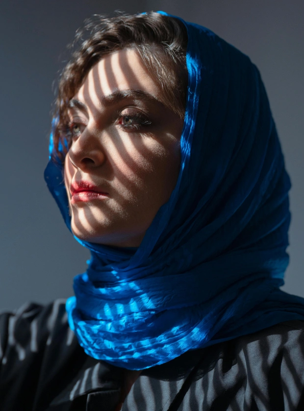 Woman wearing a vibrant blue headscarf with striped shadows cast across her face and scarf.