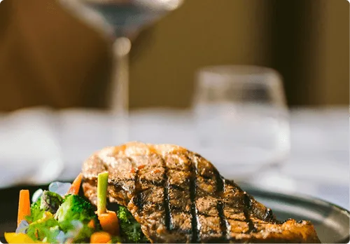 Grilled steak with mixed steamed vegetables on a dark plate.