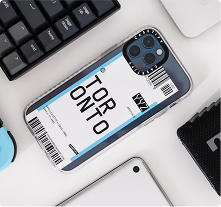 Smartphone with a clear case featuring a Toronto airport luggage tag design surrounded by keyboard, laptop, and other tech accessories.