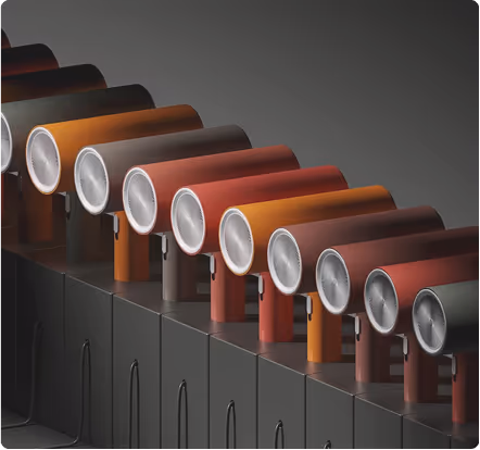 Row of vintage-style hair dryers in shades of brown, orange, and red, displayed on black cabinets against a gradient gray background.