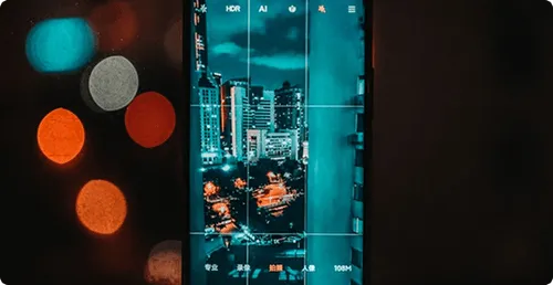 Smartphone screen displaying a nighttime cityscape being photographed, with buildings and streetlights visible.