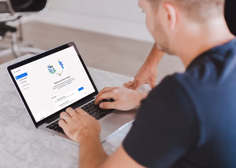 Mann bedient Laptop mit Onboarding-Software-Oberfläche auf einem weißen Tisch.