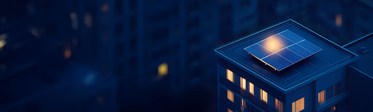 Dach eines Gebäudes mit Solarpaneelen und beleuchteten Fenstern in der Dämmerung.