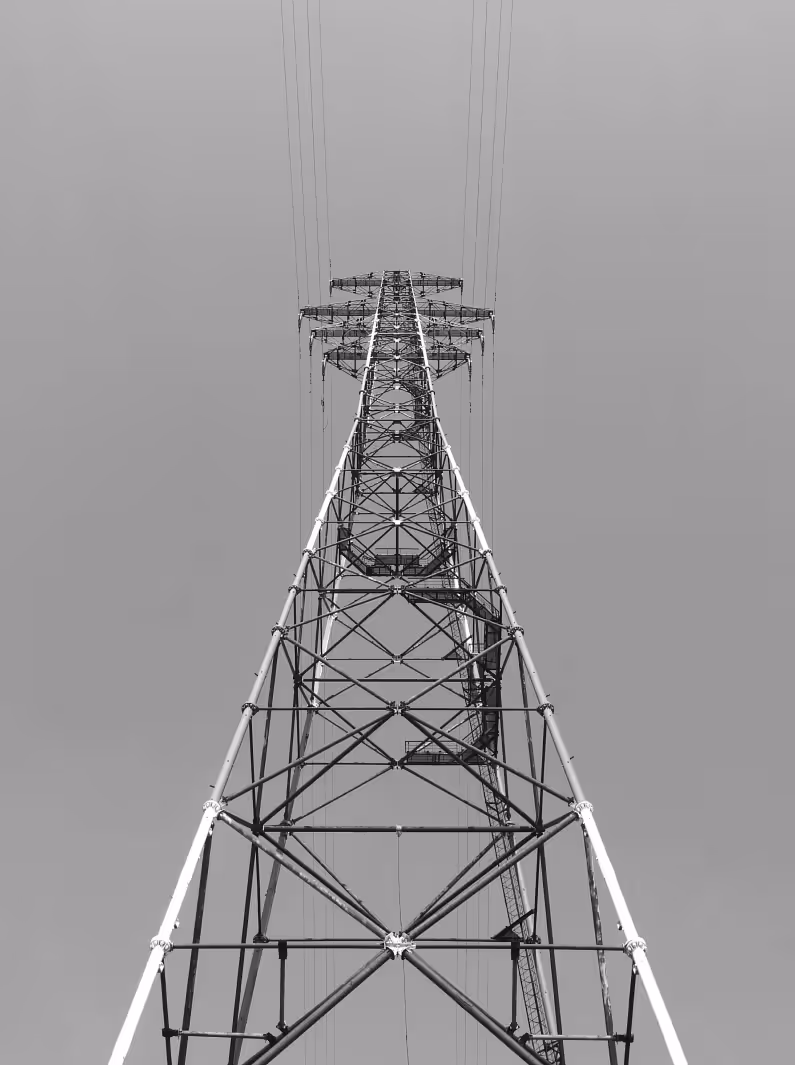 Blick von unten auf einen hohen Strommast mit Stromleitungen vor grauem Himmel.