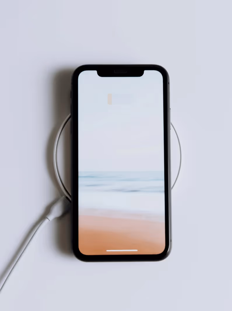 Schwarzes Smartphone, das auf einem kabellosen Ladegerät liegt, mit einem Strand- und Meeresbildschirmhintergrund.