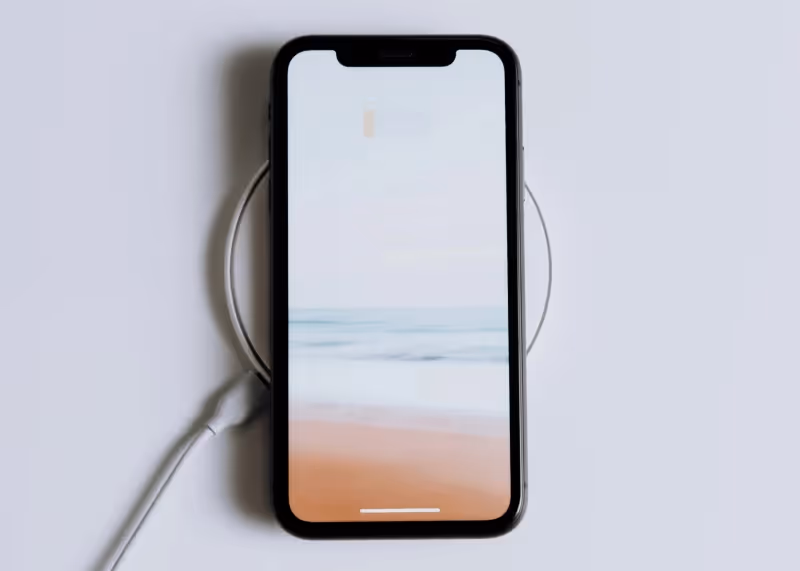 Smartphone auf einem kabellosen Ladeständer mit einem Strand- und Meeresbildschirmhintergrund.