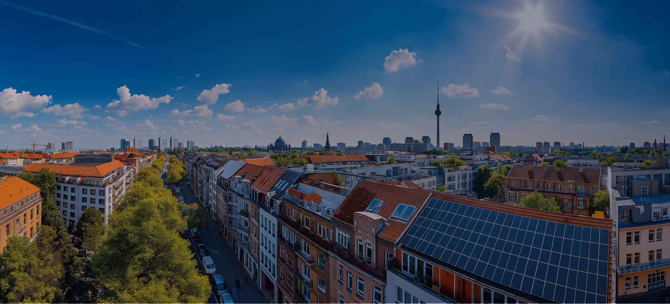 Panoramablick auf Berlins Stadtzentrum mit Sonnenlicht, Gebäuden mit Solarpaneelen und dem Fernsehturm am klaren blauen Himmel.