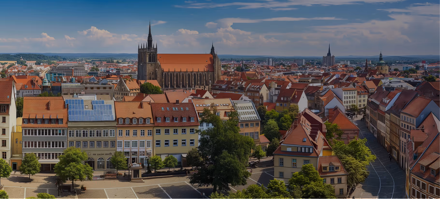 Blick über Erfurt mit der spätgotischen Severikirche und roten Ziegeldächern unter blauem Himmel.