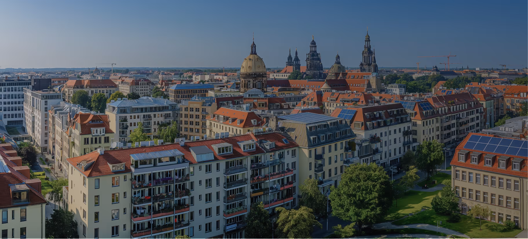 Blick auf die Stadt Dresden mit roten Ziegeldächern, historischen Kirchtürmen und moderner Architektur bei blauem Himmel.