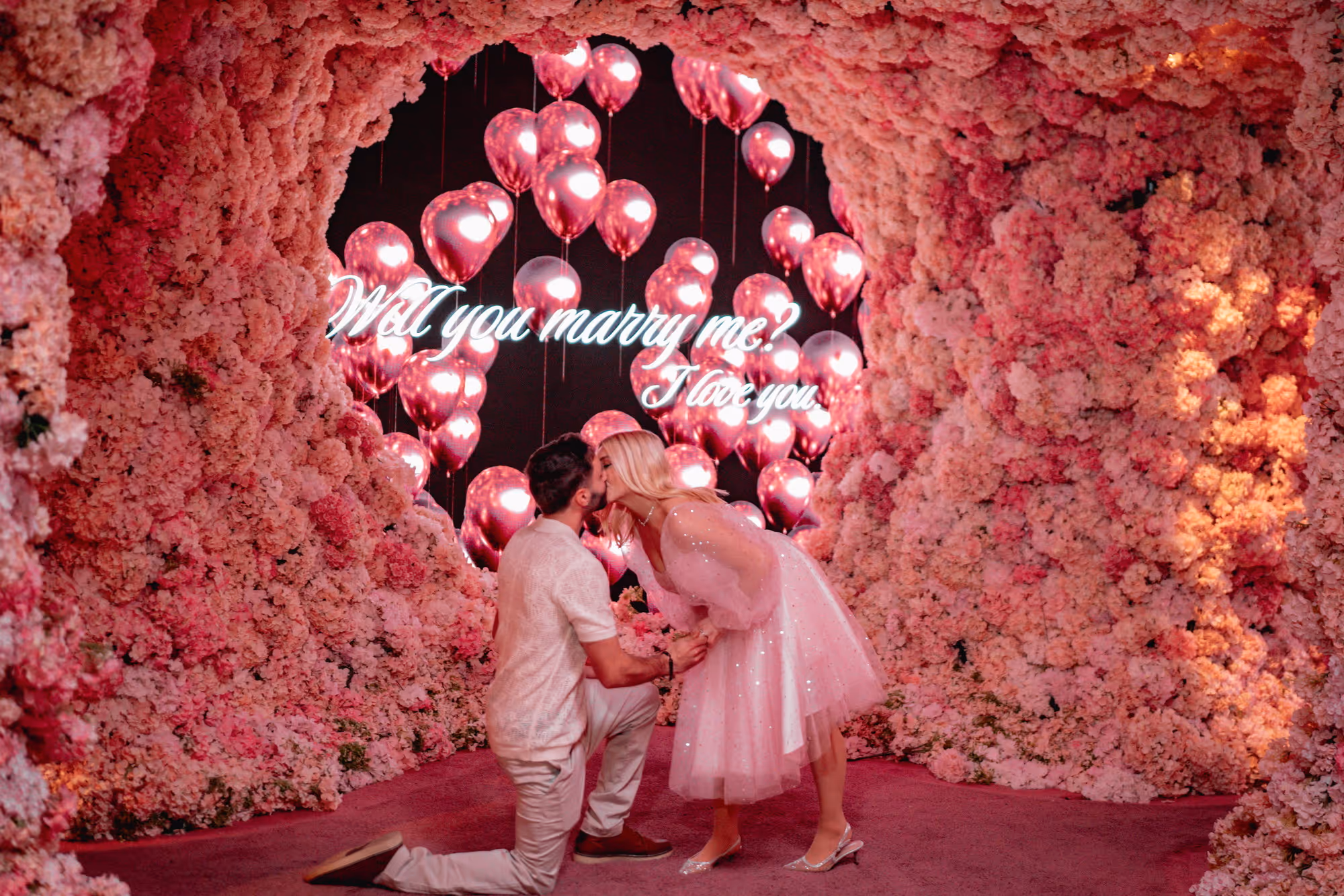 Couple kissing in the cave exhibit at Mercer Labs New York City with heart-shaped balloons and a neon sign that says 'Will you marry me? I love you.'