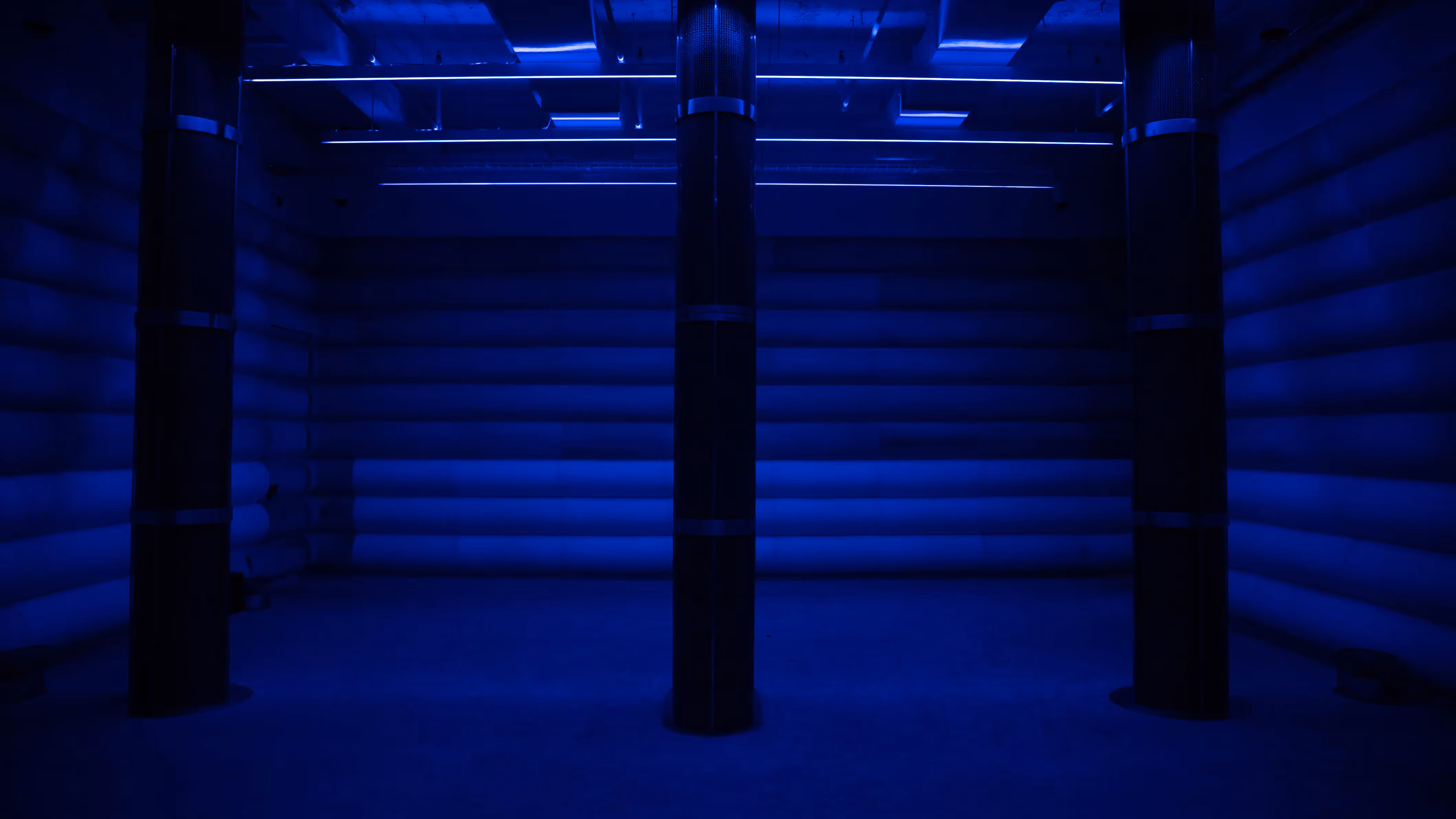 Empty inflatable sound chamber bathed in deep blue light with tall pillar speakers and horizontal LED strips along the ceiling at 4DSound, Mercer Labs in Lower Manhattan.