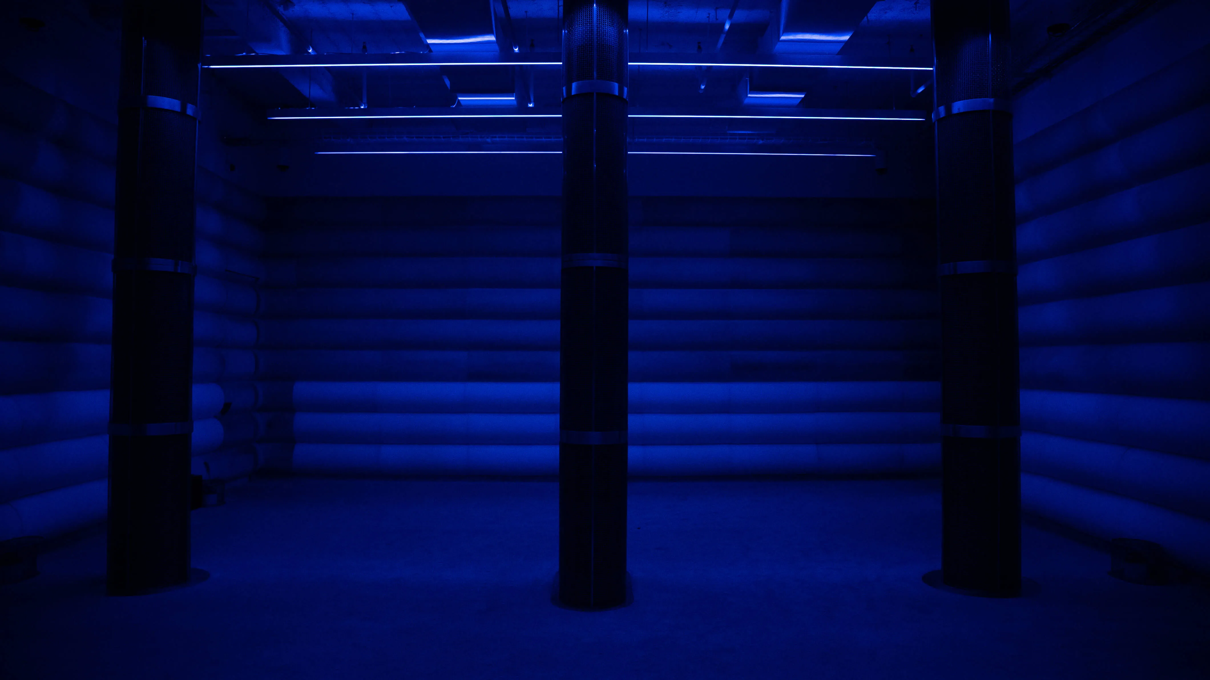 Empty inflatable sound chamber bathed in deep blue light with tall pillar speakers and horizontal LED strips along the ceiling at 4DSound, Mercer Labs in Lower Manhattan.