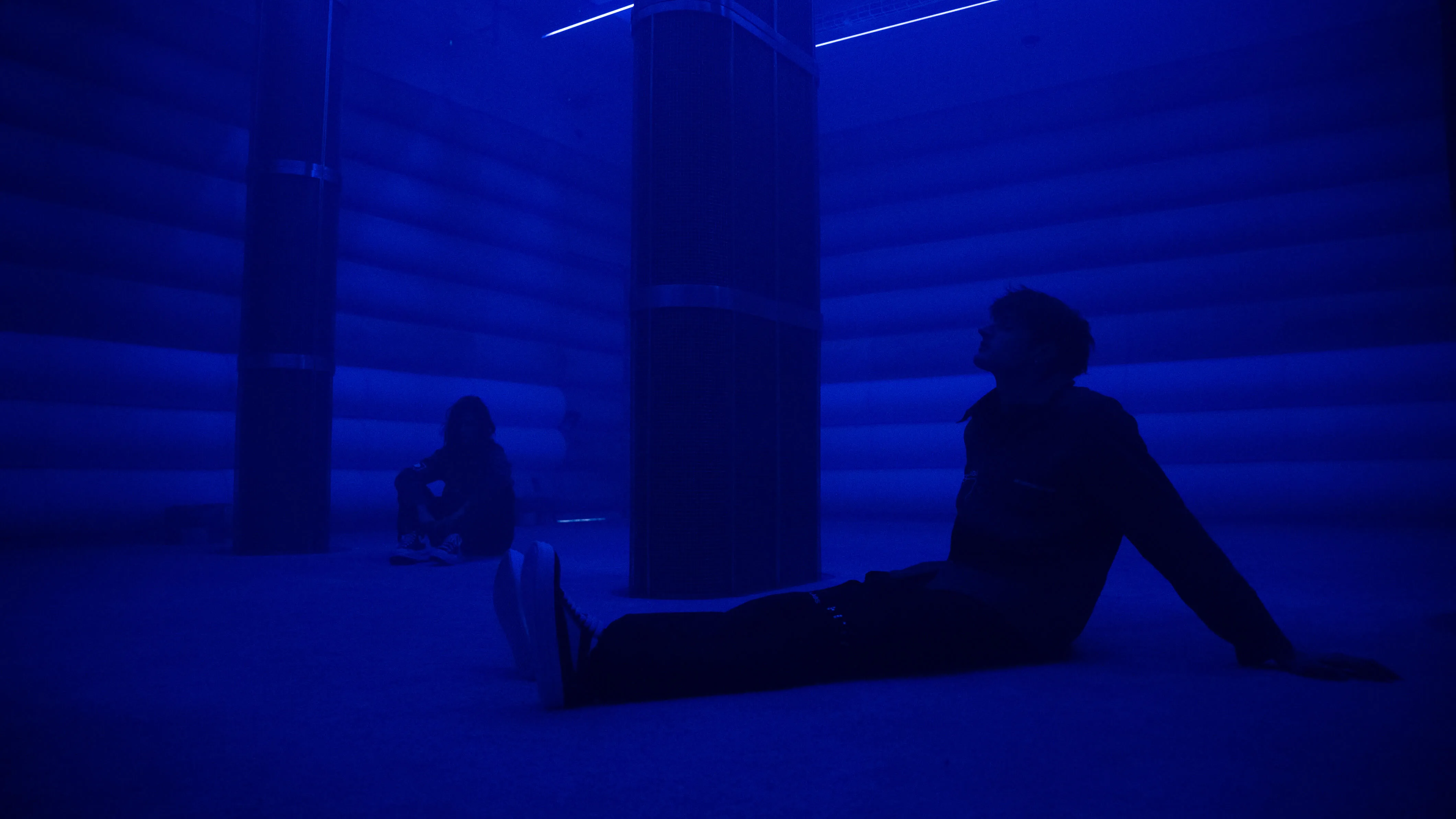Visitor reclines on the floor of the 4DSound installation, lit in deep blue inside the immersive sonic chamber at Mercer Labs, an art and science museum in NYC.