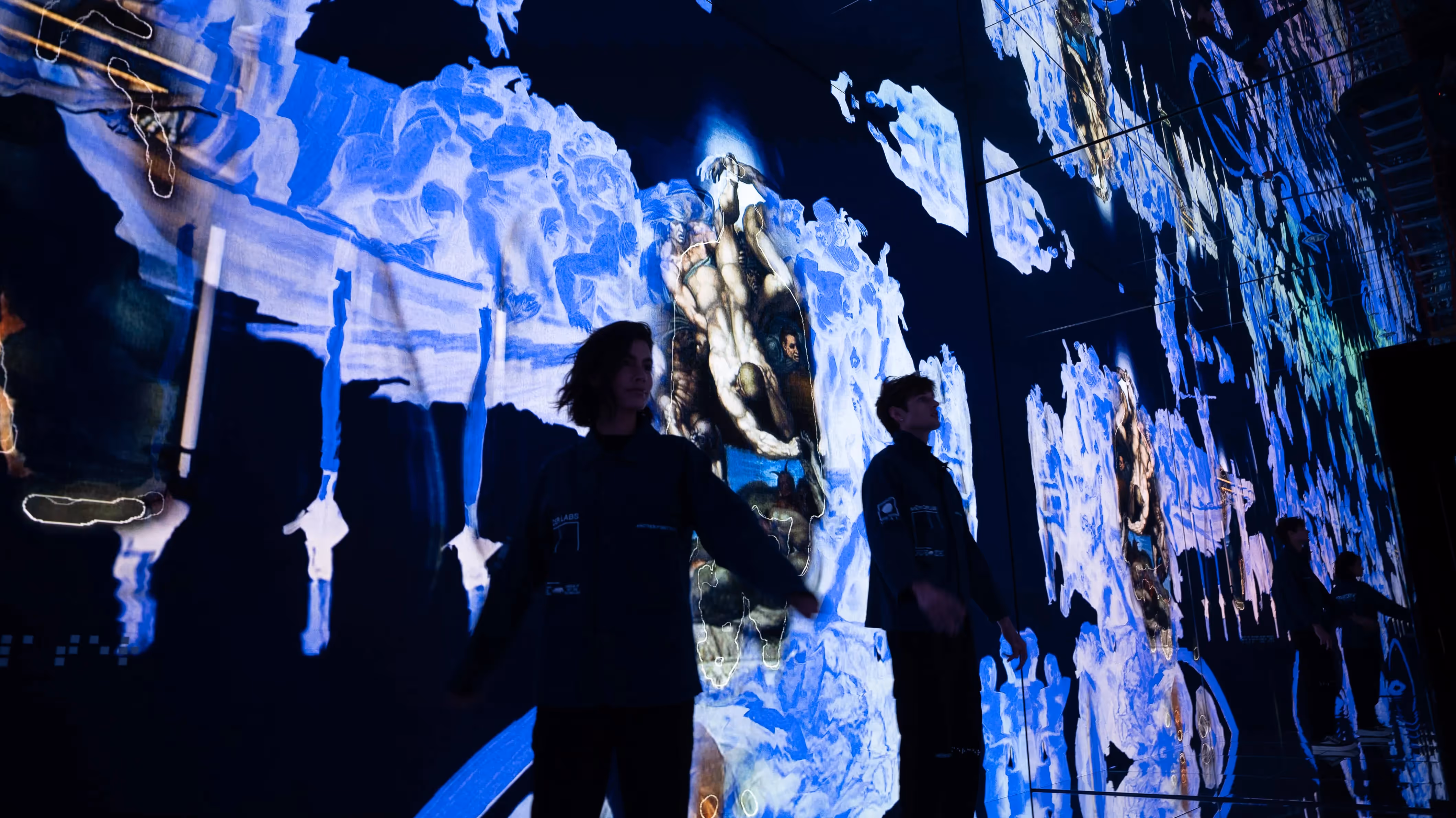 Visitors walk through the mirrored Infinite gallery at Mercer Labs, surrounded by fragmented blue and ochre projections of Michelangelo's Last Judgment, NYC.