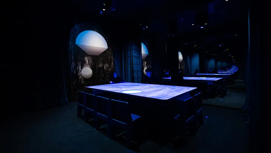Wide view of multiple illuminated blue tables extending into the mirrored Blue Room gallery at Mercer Labs, Lower Manhattan, with Venus paintings and dome lights repeated down the space.