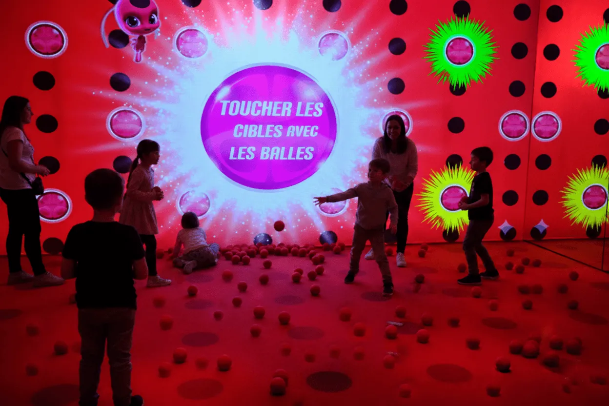 Children and adults standing and running on a pink-lit stage with hexagonal wall panels, with large text 'RÉFLEXION RAPIDE' and a green stopwatch icon in the center.