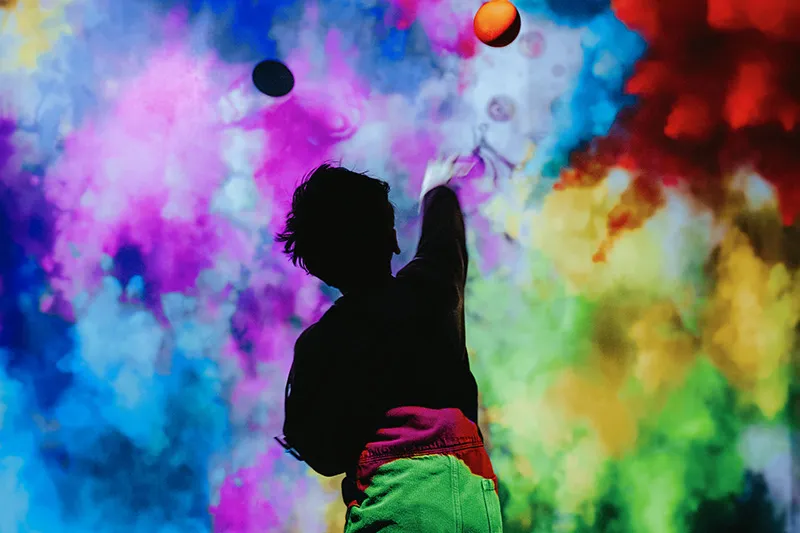 A child reaching up towards a large screen displaying a character in a red and black spotted superhero costume with the word 'FÉLICITATIONS' above them.