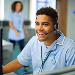 Smiling healthcare worker wearing a headset and scrubs in a medical office.