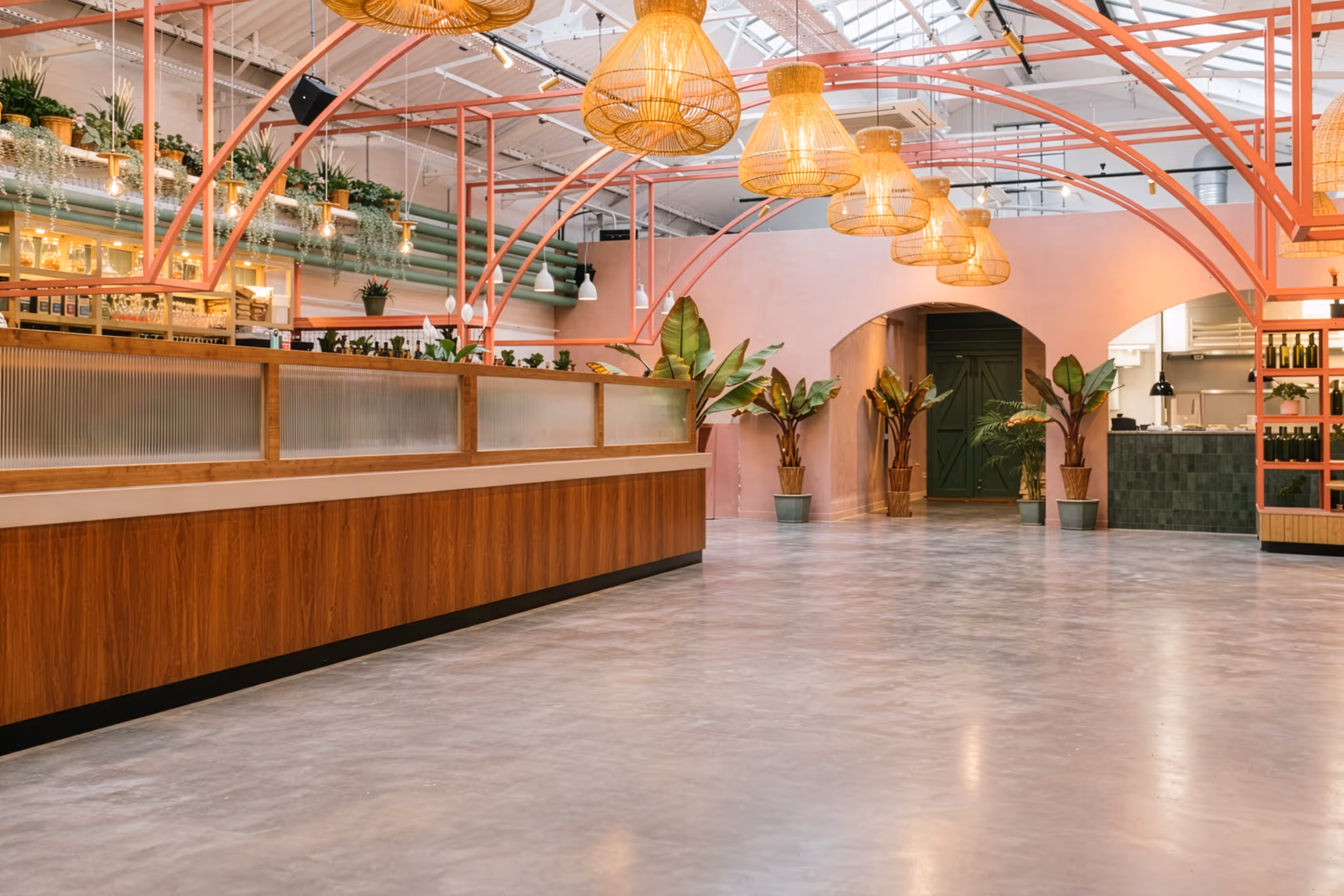 Spacious modern interior with pink arches, large hanging wicker lamps, green potted plants, and wooden counters.