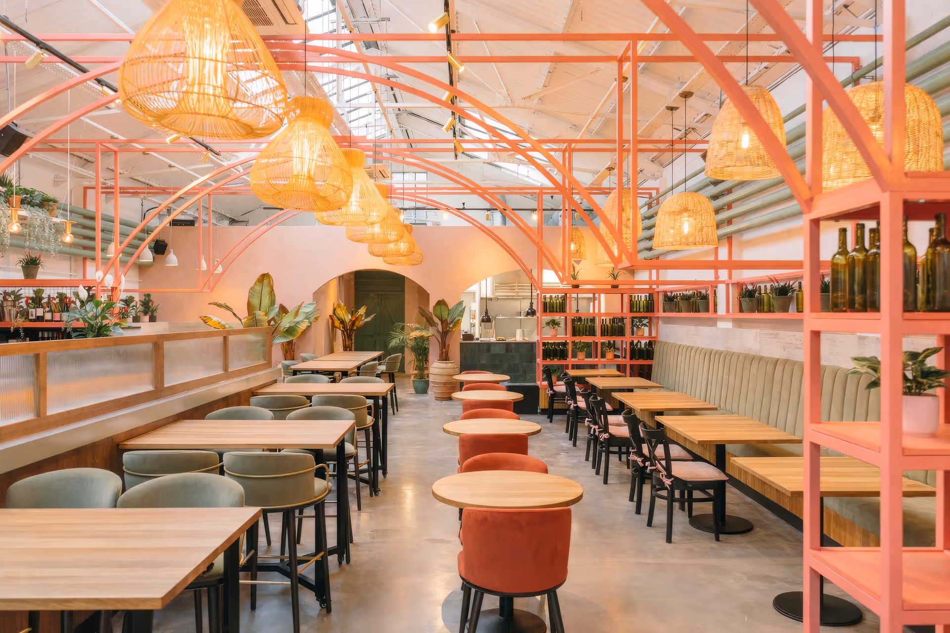 Bright, modern restaurant interior with wooden tables, green and orange chairs, pink metal frames, and warm hanging wicker lights.