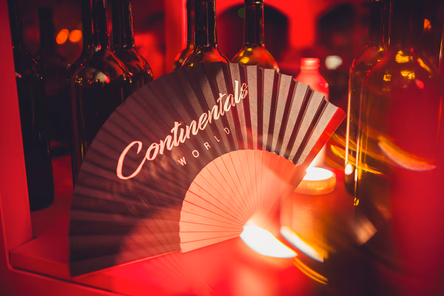 Decorative fan with the words 'Continental World' placed among glass bottles illuminated by warm red and orange lighting.