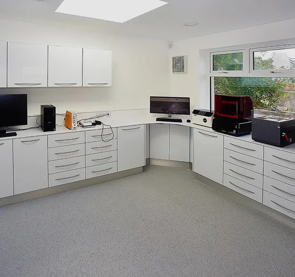Modern clean laboratory room with white cabinets, countertops, computer monitors, and scientific equipment near a window.