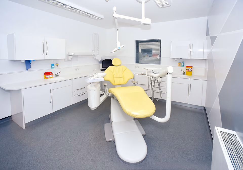 Modern dental examination room with a yellow dental chair and surrounding white cabinets.