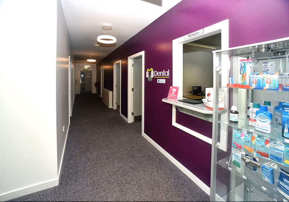 Hallway in a dental clinic with purple walls, a reception window, and a glass display case with dental products.