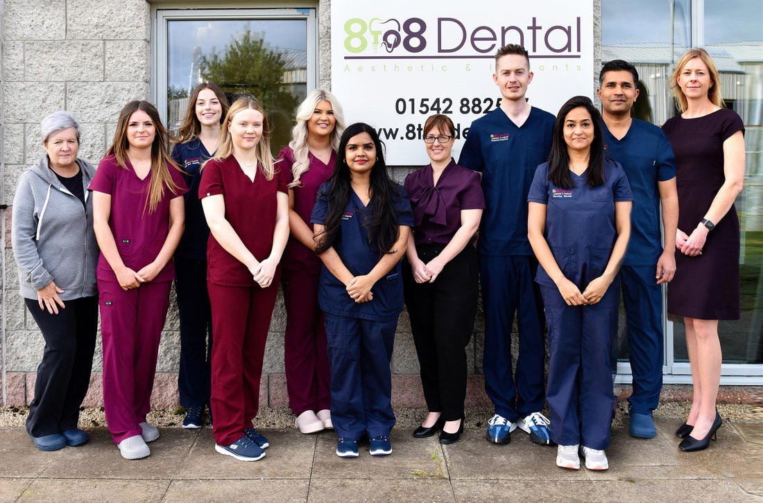 Group photo of dental clinic staff standing outside the 818 Dental clinic sign, dressed in scrubs and professional attire.