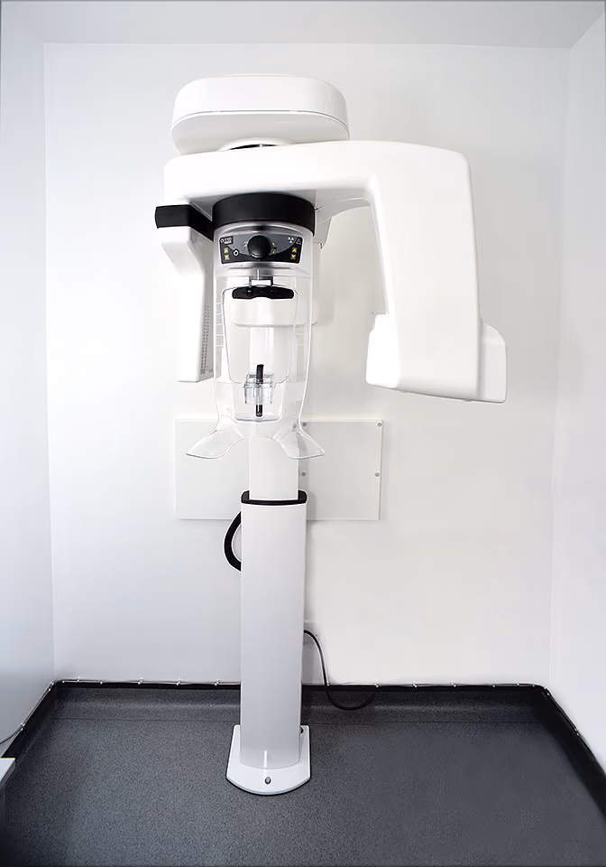 Modern dental panoramic X-ray machine mounted on a white wall in a clinical setting.