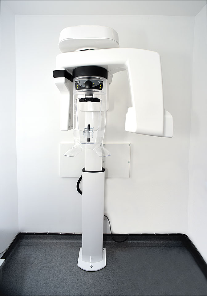 Modern dental panoramic X-ray machine mounted on a white wall in a clinical setting.
