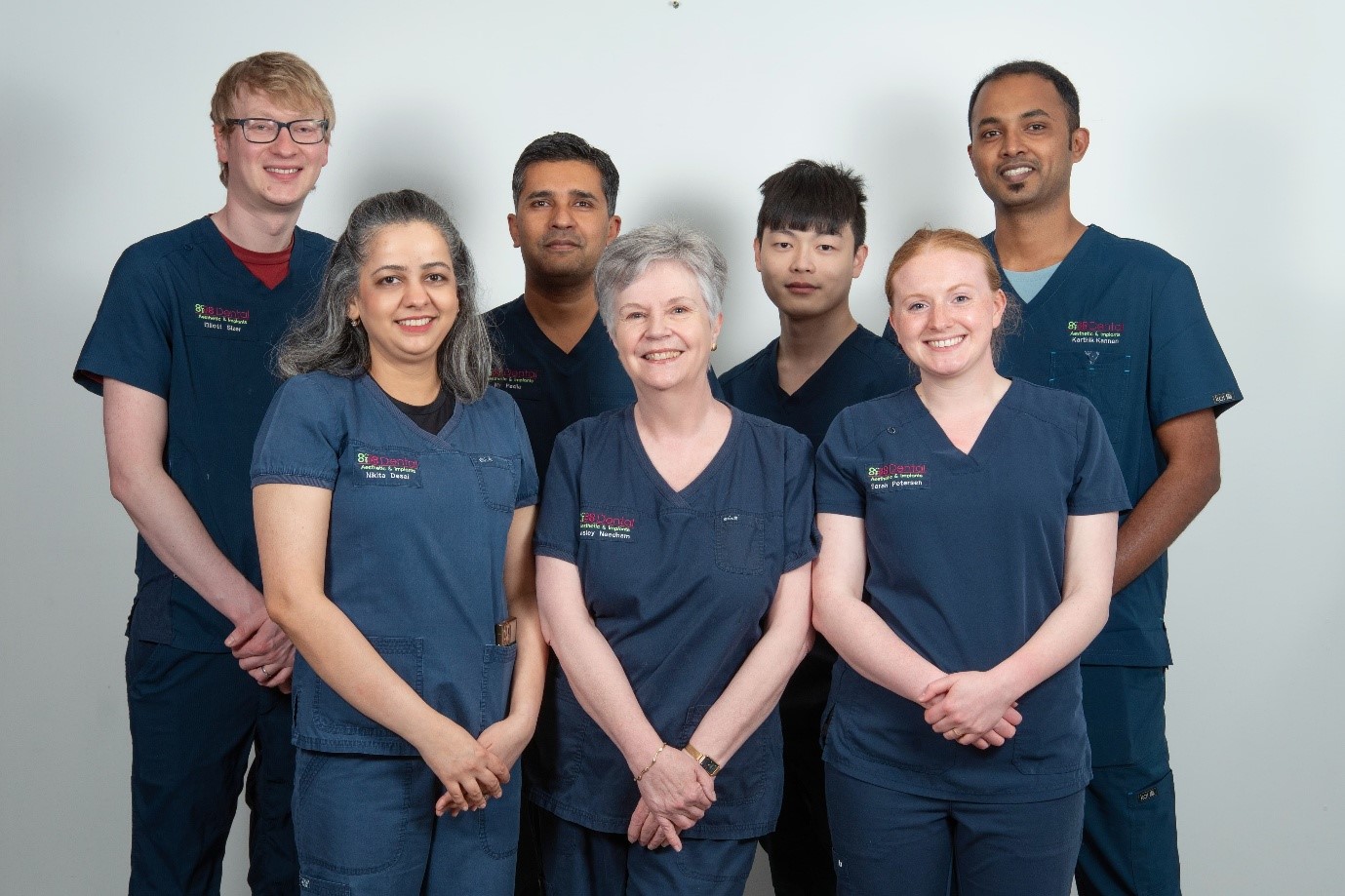 Group portrait of six healthcare professionals in navy scrubs standing against a plain background, smiling at the camera.