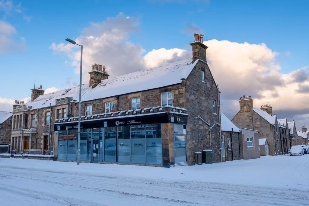 Snow-covered stone buildings on a street under a partly cloudy sky during winter.