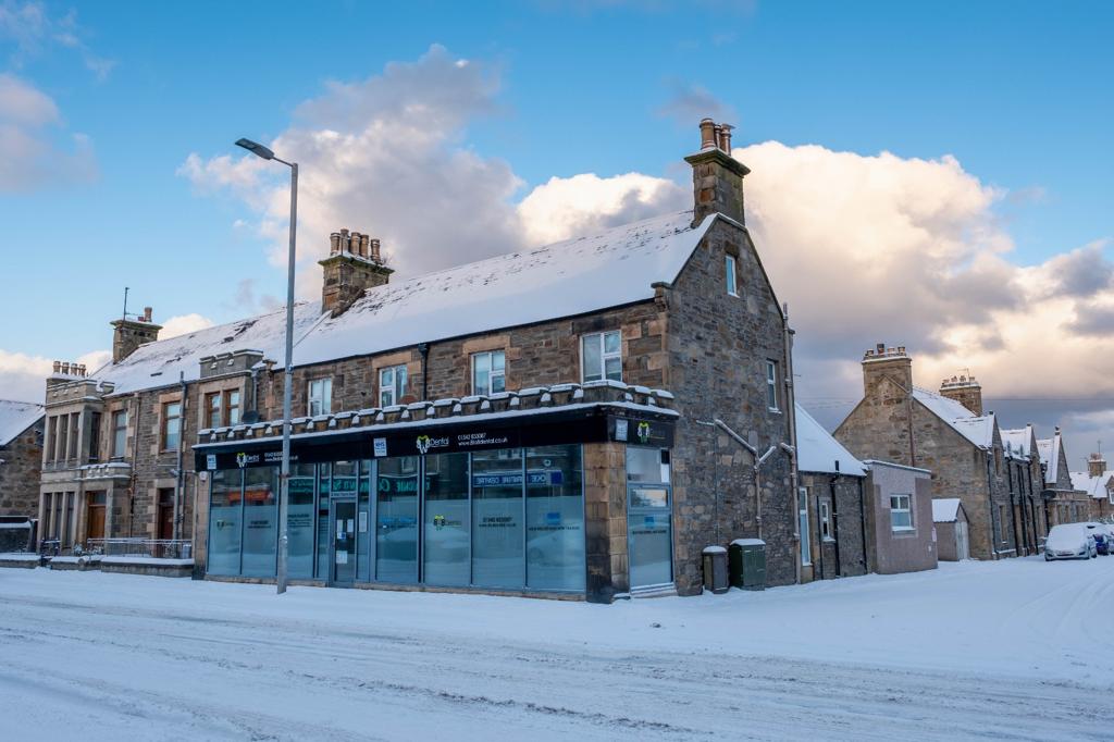 Snow-covered stone buildings on a street under a partly cloudy sky during winter.