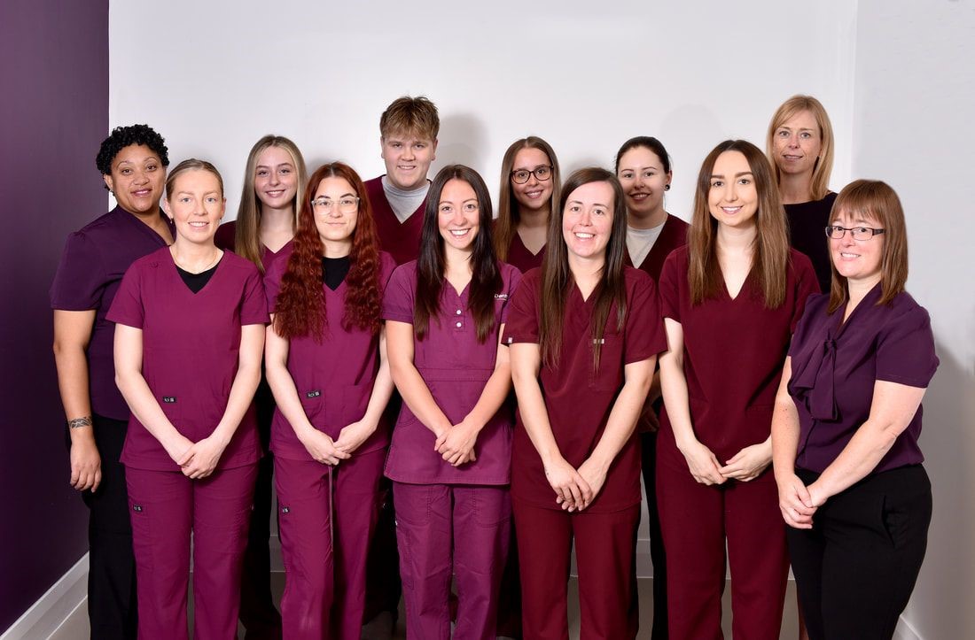 A group of twelve medical or dental professionals in matching maroon scrubs posing against a white and purple wall.