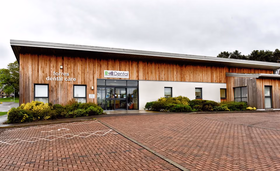 Modern building with wooden paneling and a sign reading 'forres dental care' and '888 Dental' above the entrance with a brick parking lot in front.