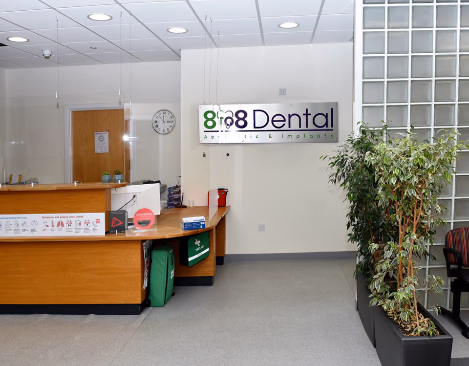 Dental clinic reception desk with protective plexiglass, clock, and 8to8 Dental sign on the wall.