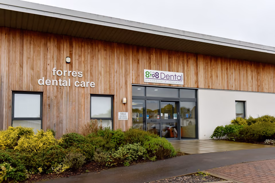 Modern dental care clinic building with wooden exterior walls, signage reading 'forres dental care' and '8788 Dental Aesthetic & Implants' above the glass entrance doors.
