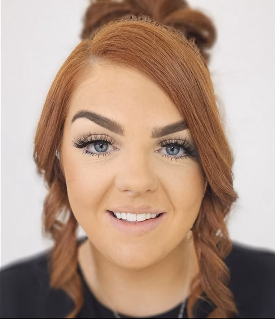 Close-up portrait of a smiling woman with red hair styled in loose curls and striking blue eyes.
