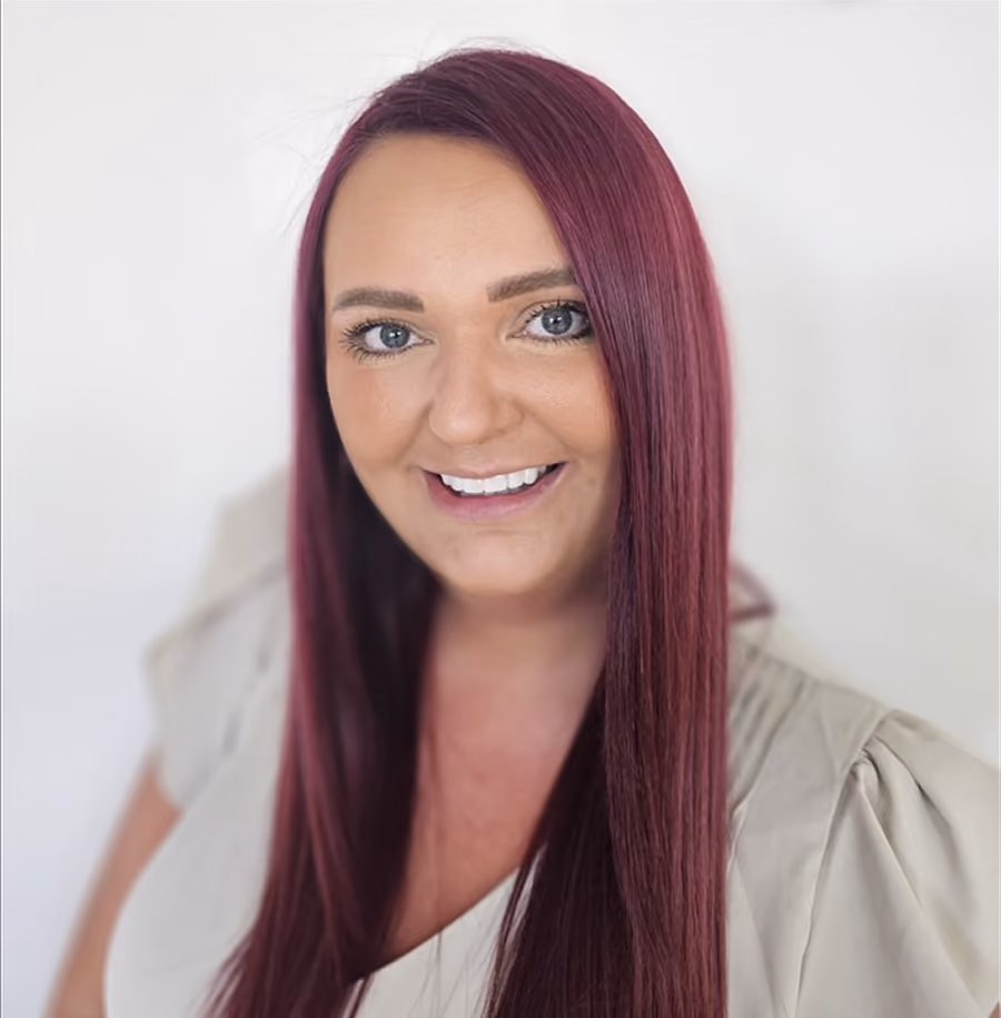 Smiling woman with long straight burgundy hair wearing a light-colored top against a plain white background.