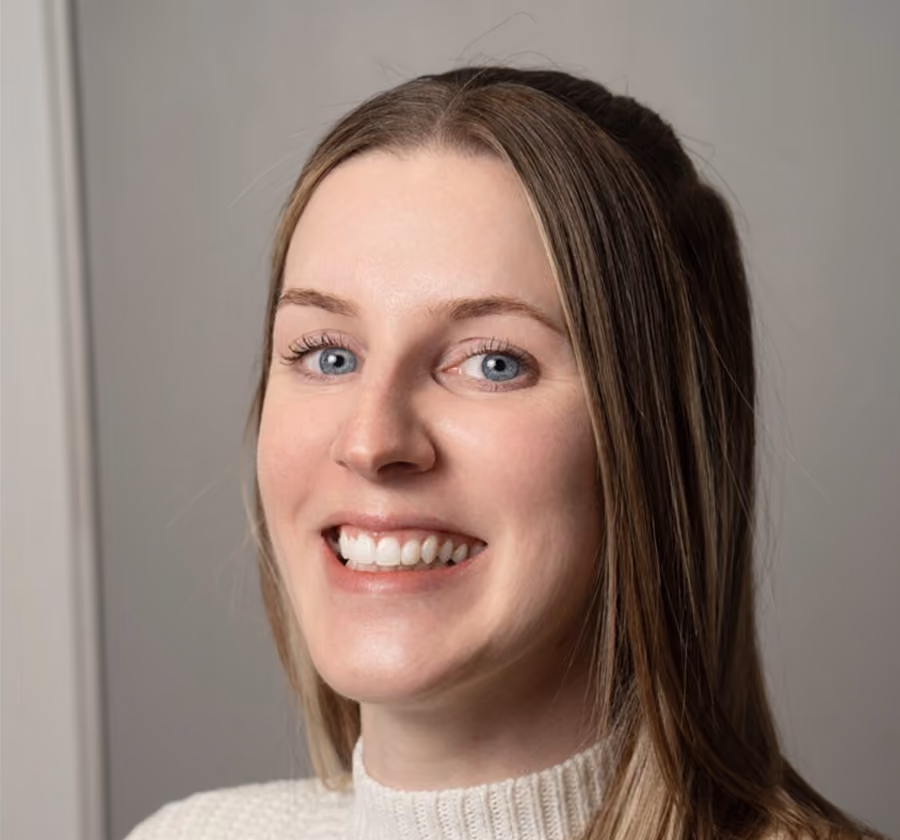 Smiling woman with long light brown hair and blue eyes wearing a white knit sweater against a plain background.