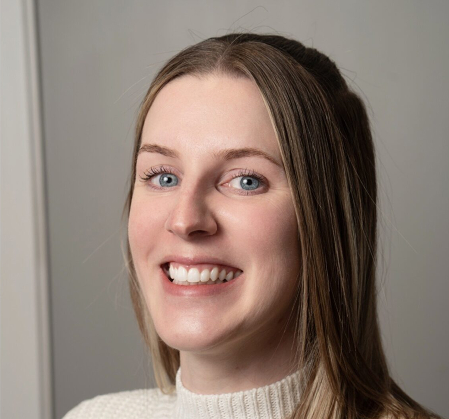 Smiling woman with long light brown hair and blue eyes wearing a white knit sweater against a plain background.