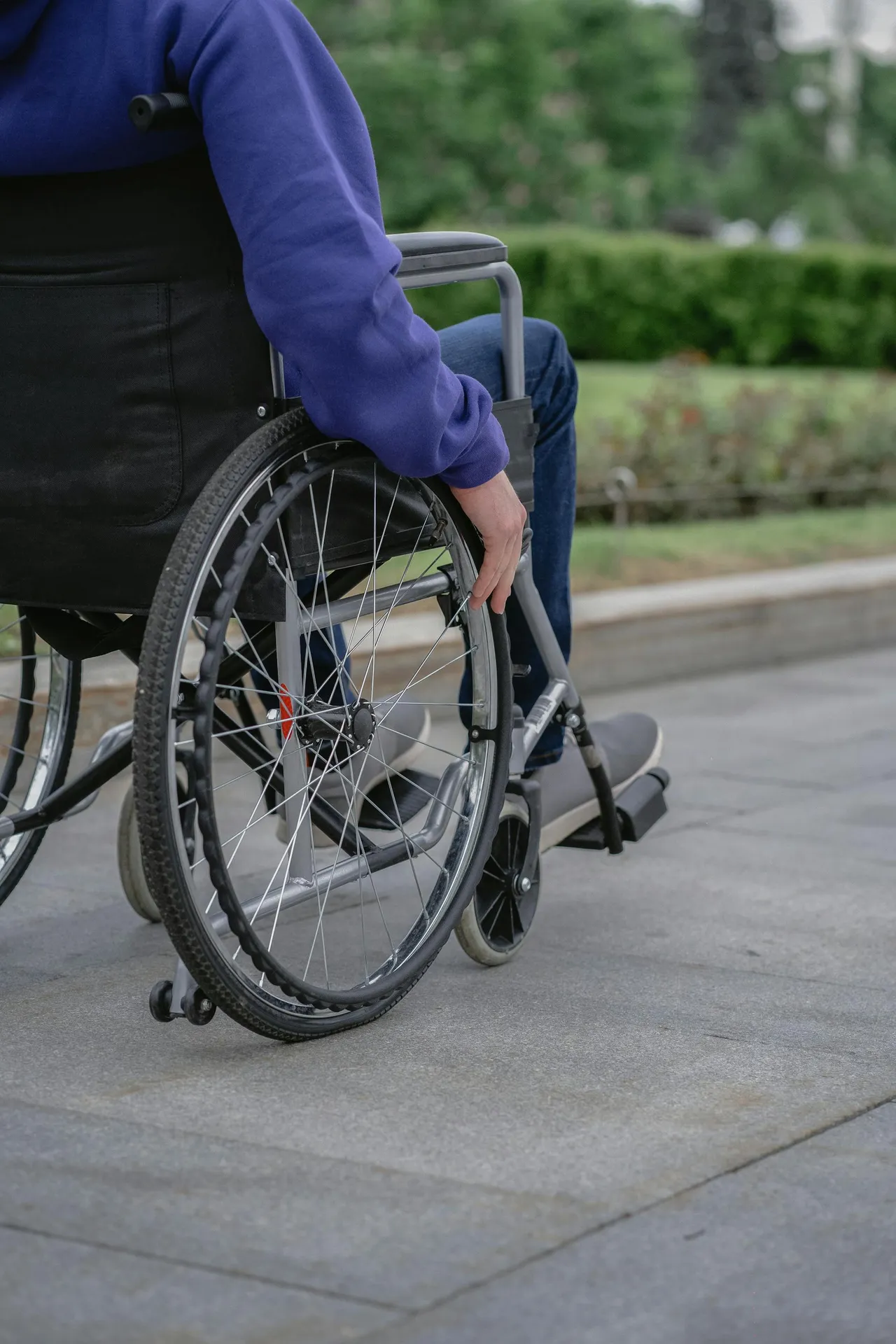 Person in a wheelchair outdoors on a paved path with greenery in the background.