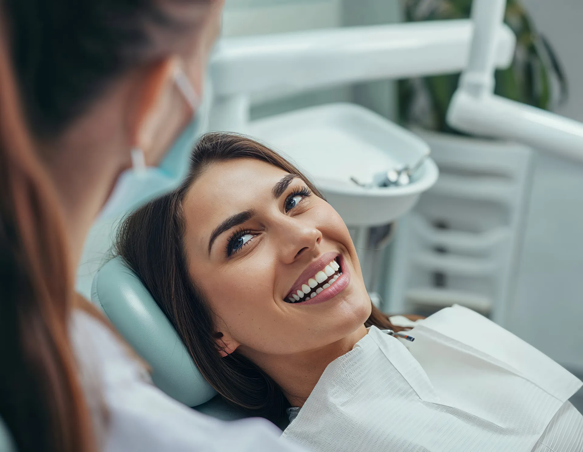 Smiling woman lying back in a dental chair looking at a masked dentist.