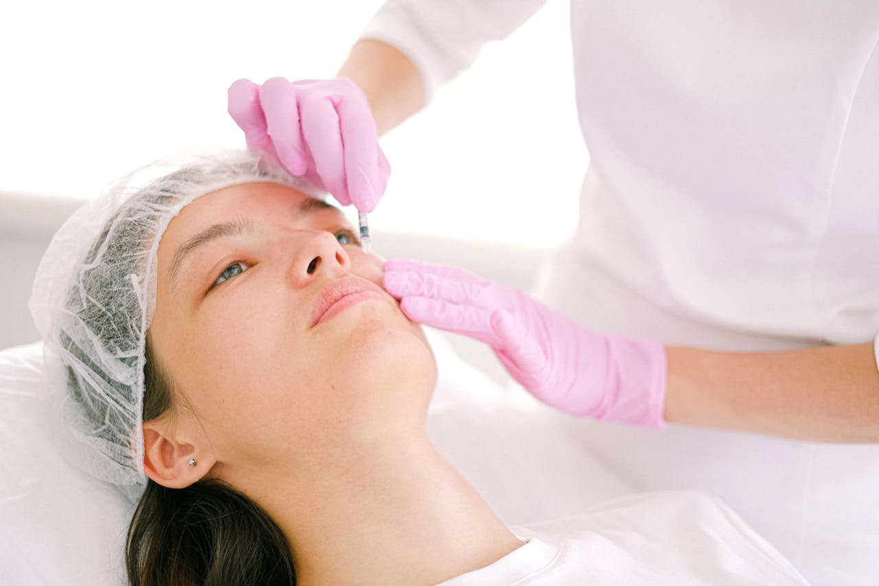 Close-up of a woman receiving a cosmetic injection in her cheek by a professional wearing pink gloves.