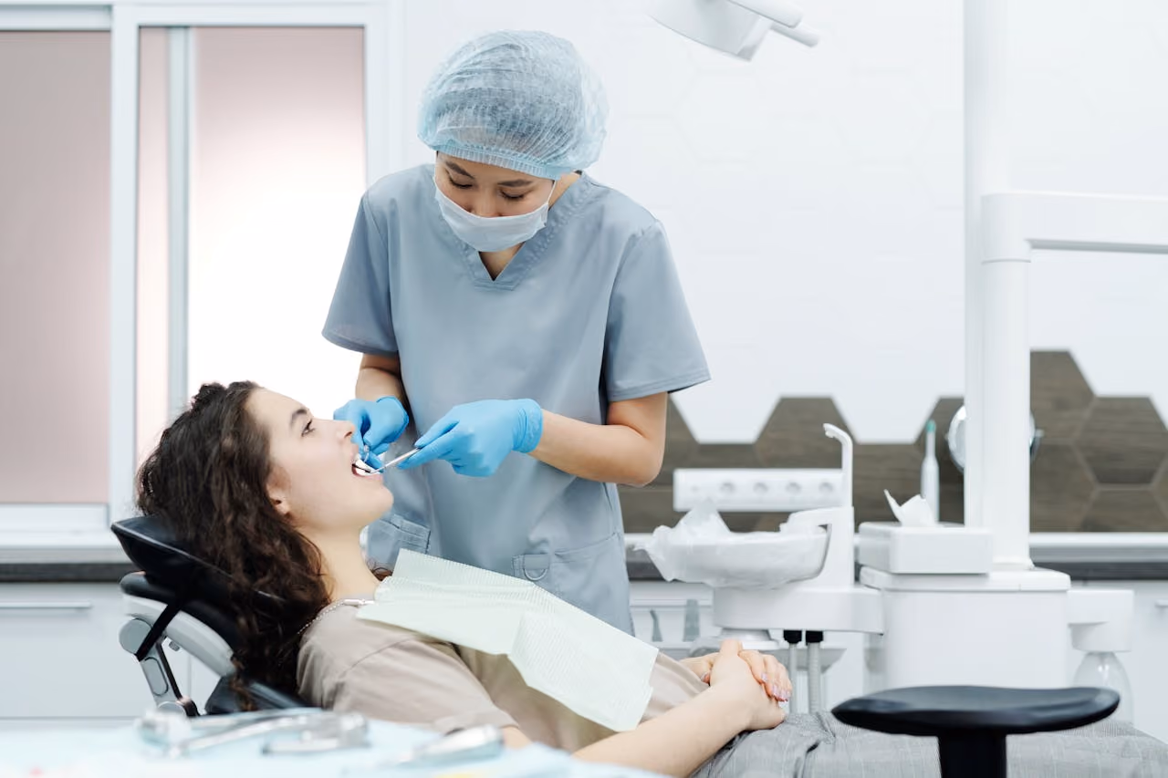 Dentist wearing mask and gloves examining a patient's teeth in a modern dental clinic.