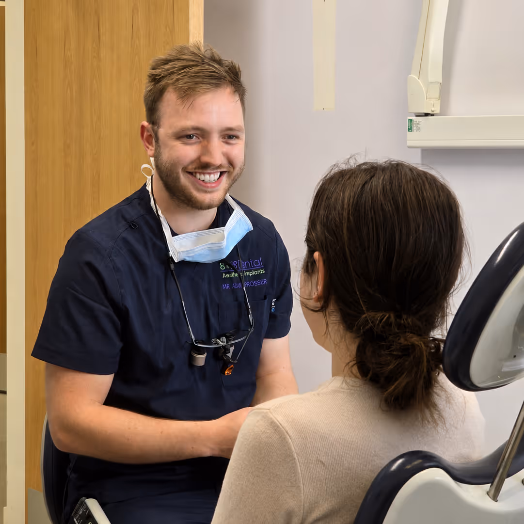 Male dentist smiling and talking to a female patient seated in a dental chair.