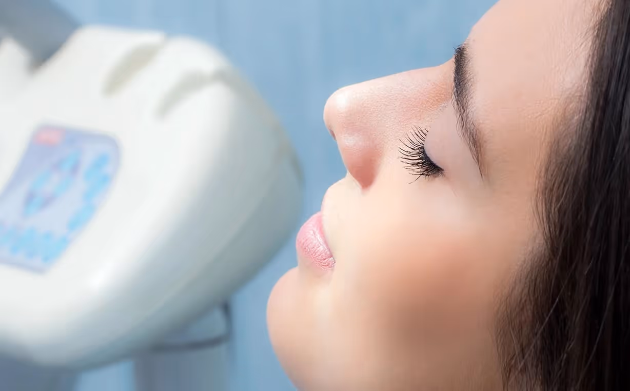 Close-up profile of a woman's face with eyes closed near a white medical or dental device.